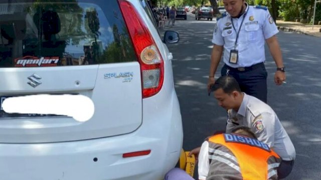 Petugas Dishub Makassar saat menggembok mobil yang parkir di bahu jalan.